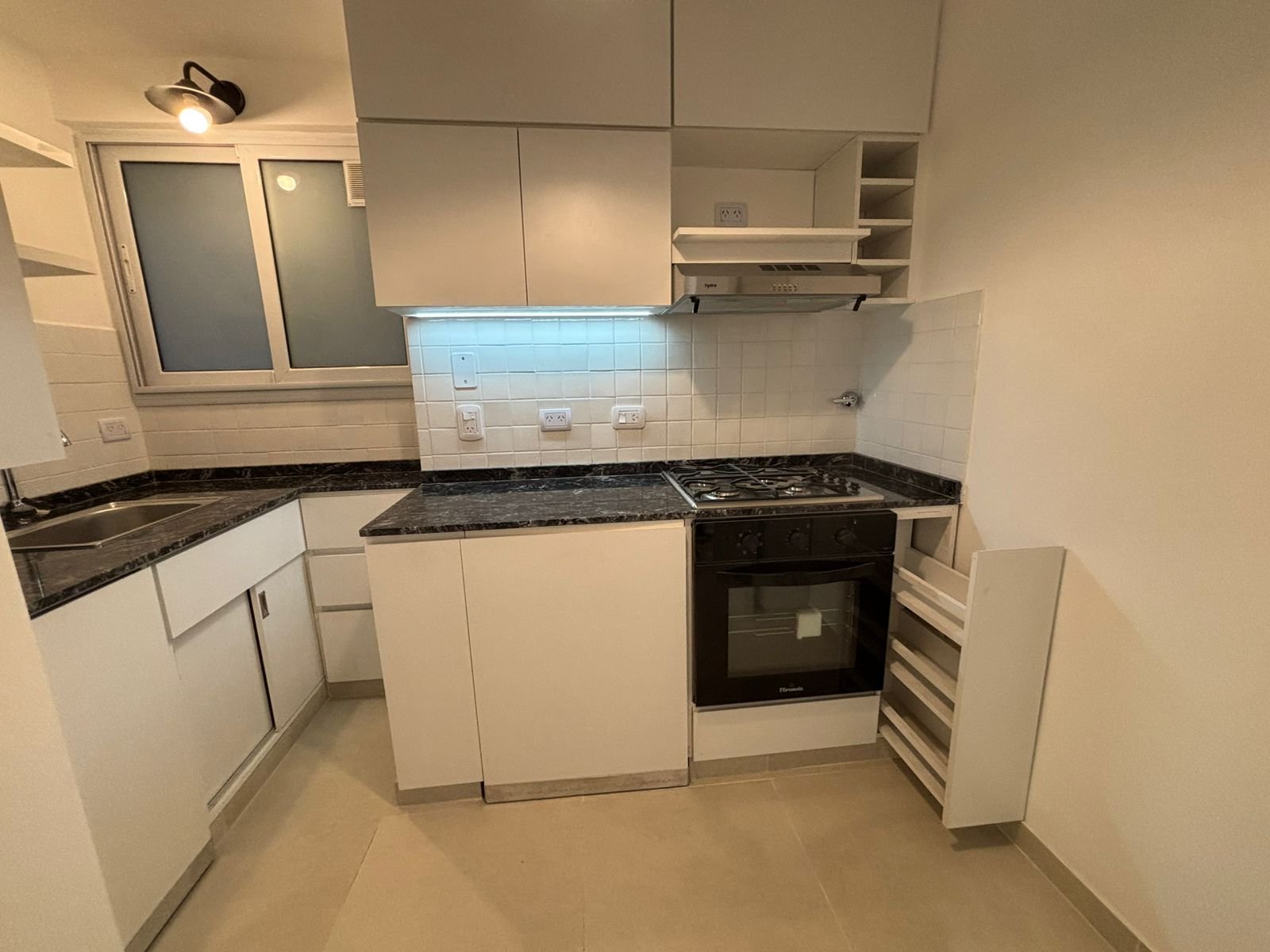 Cocina moderna blanca con encimeras de mármol y electrodomésticos negros — proyecto Depto Almagro, por Ailén Lucero Arquitectura, en Almagro